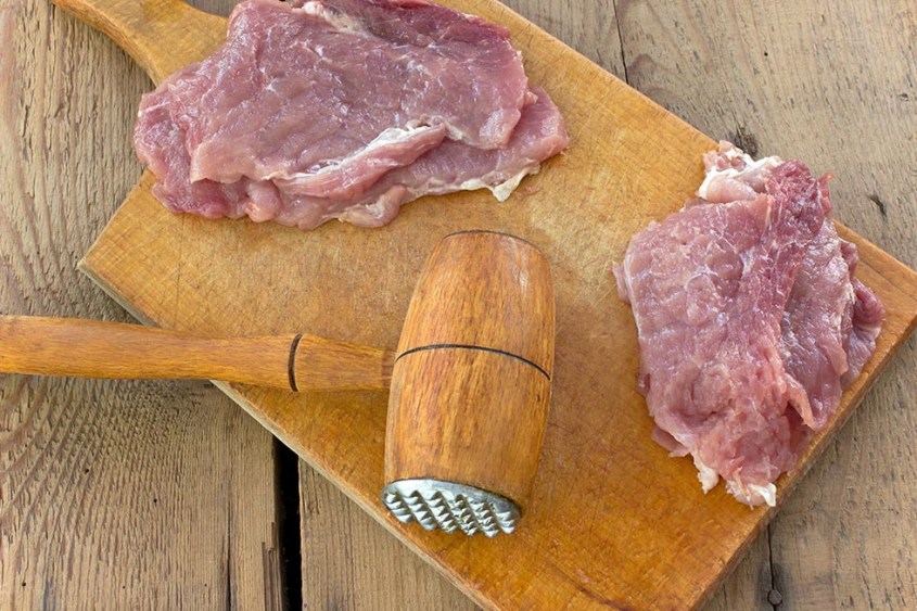 Tenderize slabs of meat on wooden board